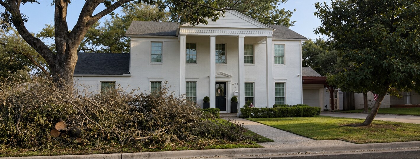 White colonial home with overgrown brush piled on the lawn before the project